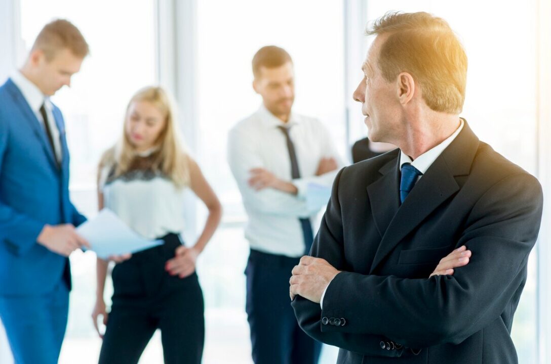 dojrzaly biznesmen patrzeje jego kolegow w biurze z faldowymi rekami 23 2147900021